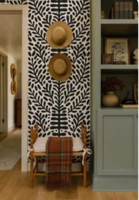 Hallway with leaf-patterned wallpaper, two straw hats hung above a wooden bench and a plaid wool throw
