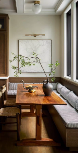 Built-in banquette with striped cushions, a wooden trestle table and a branch in a dark ceramic pitcher