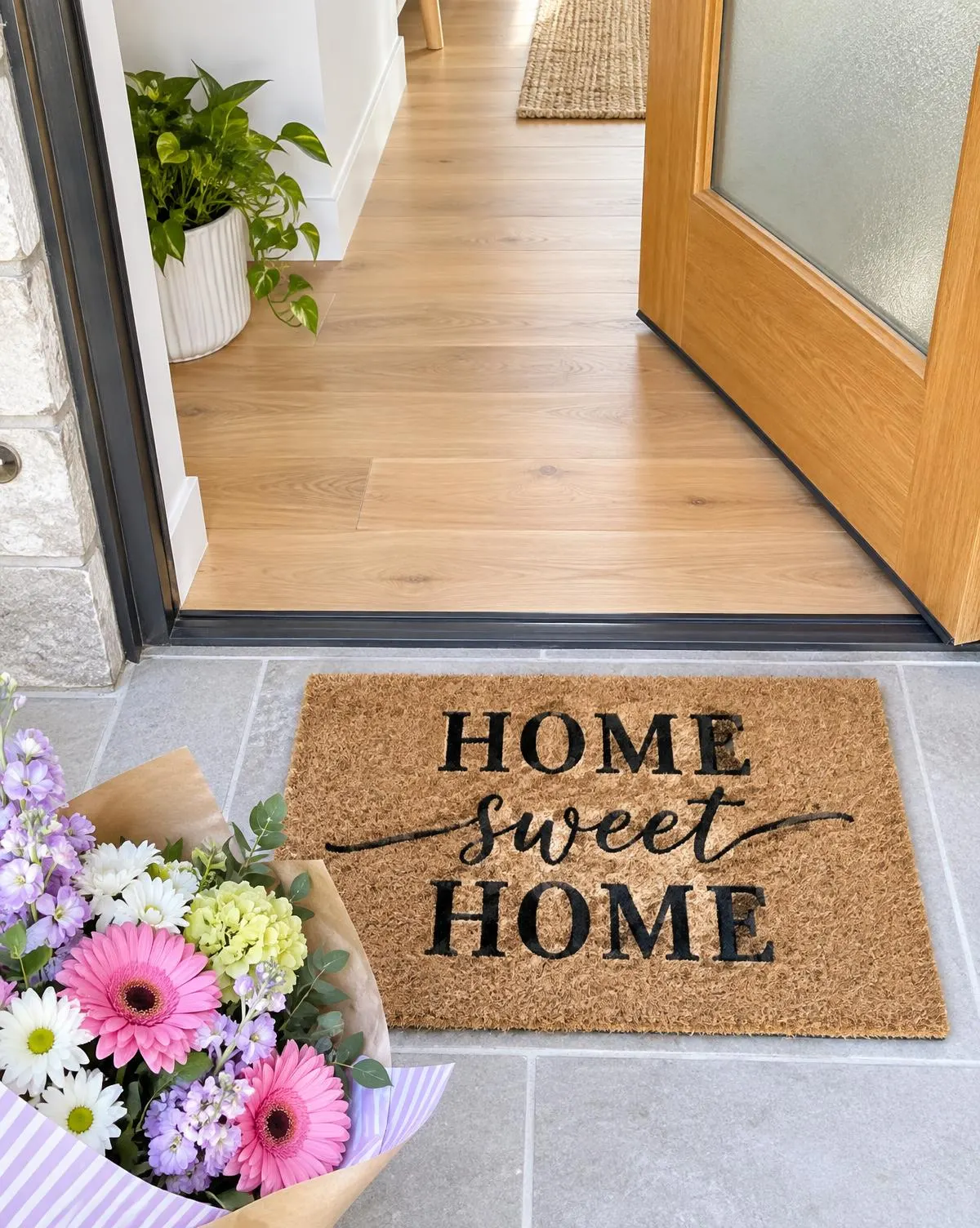 A Home Sweet Home doormat and a bouquet of flowers at an open front door