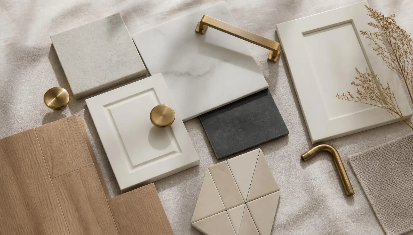 Stone, tile, oak flooring, and brass hardware samples arranged on pale linen in natural light