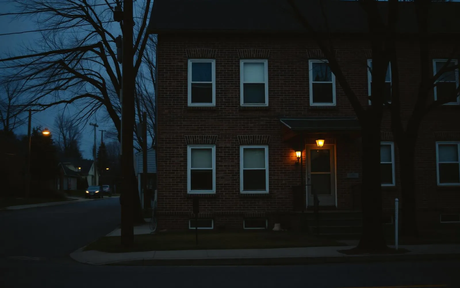 A brick duplex on a quiet street at dusk with porch lights on